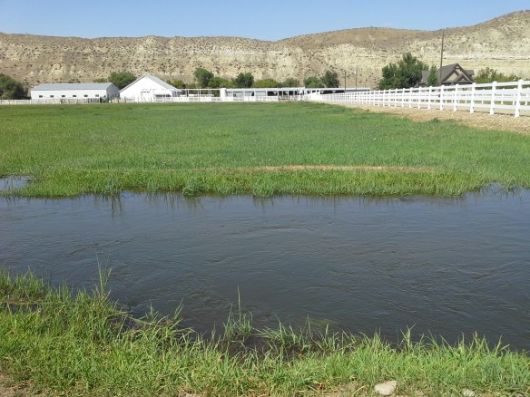 Across Highway 52 to the north, working ranches, community irrigation canals, and distantly recognizable sandstone cliffs and bluffs lie in close proximity to the directionally drilled and potentially fracked Smoke Ranch natural gas well, within a river confluence and wetlands floodplain.