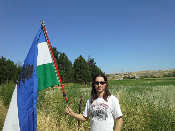 Indigenous activist and defender of wolves, Mato Woksape, flies the Cascadia flag at the last stop of a great educational and expressive event, as concerned Idaho citizens converge along Little Willow Road, to view the drilling derrick and operations of the ML Investments 2-10 well, situated on a private road and property.