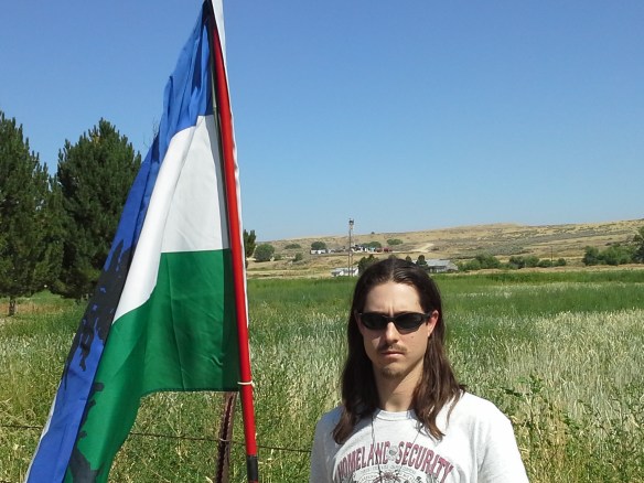 Indigenous activist and defender of wolves, Mato Woksape, flies the Cascadia flag at the last stop of a great educational and expressive event, as concerned Idaho citizens converge along Little Willow Road, to view the drilling derrick and operations of the ML Investments 2-10 well, situated on a private road and property.